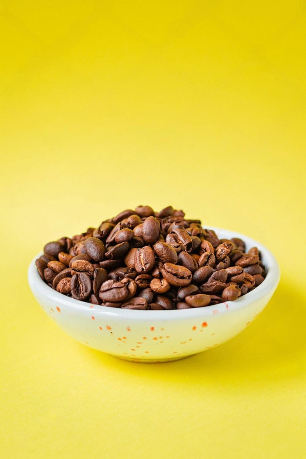 White ceramic bowl filled with roasted Arabica and Robusta coffee beans on a yellow background