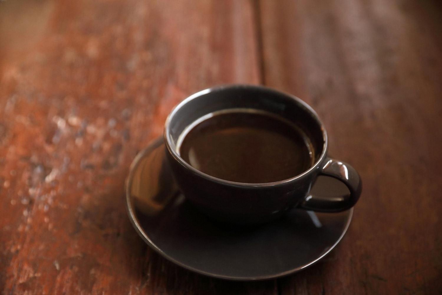 Dark cup of freshly brewed black coffee on a wooden table